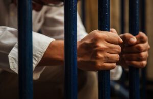 A person sits behind bars after a white collar crime charge. Penalties can include prison time and fines, depending on the charges and case details.